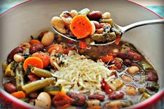 a red bowl filled with beans, carrots and other vegetables next to a spoon