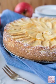 an apple pie with powdered sugar on top sits on a blue napkin next to silverware