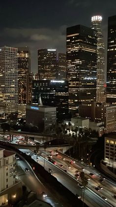 the city skyline is lit up at night with cars driving down it's street