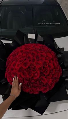 a woman's hand is holding a large bouquet of red roses in front of a white car