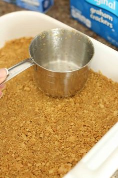 a person scooping something out of a white dish with a metal measuring spoon in it