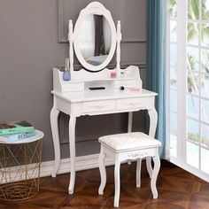 a white dressing table with mirror and stool in front of a window on a wooden floor