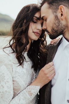 a man and woman standing next to each other in front of the ocean with their eyes closed