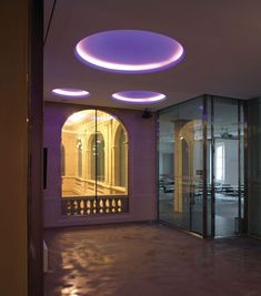 an empty room with glass walls and purple lighting on the ceiling is lit up by circular lights