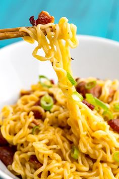 the noodles are being held up by chopsticks in a white bowl with bacon and green onions