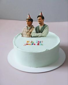 two men sitting on top of a white cake with the words happy birthday written on it