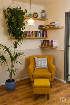 a yellow chair sitting in front of a book shelf filled with books and a potted plant