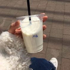 a person holding a plastic cup with milk in it's hand on the sidewalk