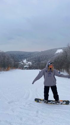 a person on a snowboard in the snow with trees and hills behind them,