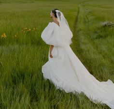 a woman in a wedding dress walking through tall grass