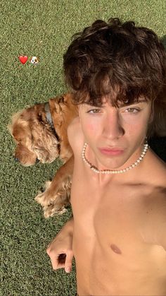 a shirtless man laying on the ground next to a brown dog wearing a pearl necklace