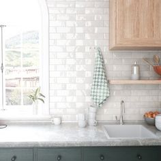 a kitchen with green cabinets and white tiled backsplash, an open window to the outside