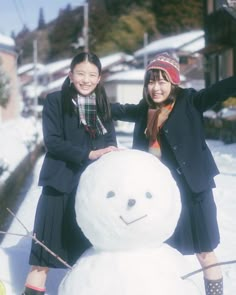 two girls standing next to a snowman in the snow