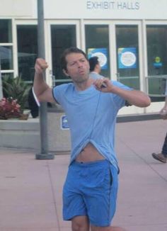 a man in blue shirt and shorts playing with a frisbee on the sidewalk