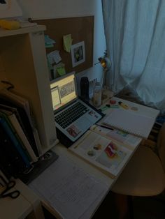 an open laptop computer sitting on top of a desk next to a pile of papers