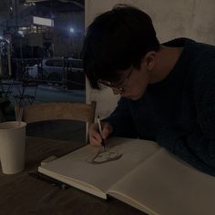 a person sitting at a table with a book and pen in front of them, writing