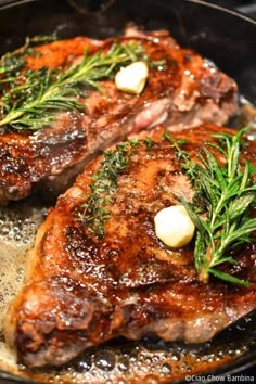 two steaks cooking in a skillet with herbs on top