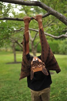 a person hanging upside down on a tree branch with their hands in the air while wearing a mask