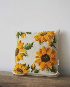 a pillow with yellow sunflowers on it sitting on top of a wooden shelf