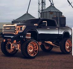 a black truck with gold rims parked in front of a grain silo and windmill