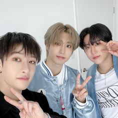 three young men standing next to each other in front of a white wall and pointing fingers at the camera