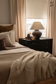 a bed sitting under a window next to a night stand with a lamp on it