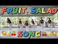 a group of people that are standing in front of a sign with fruit salad on it