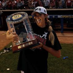 a woman holding a trophy on top of a baseball field