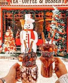 two people holding up mugs in front of a store decorated with christmas trees and decorations