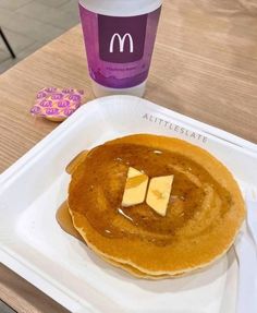 pancakes with butter and syrup on a white plate next to a cup of ice cream