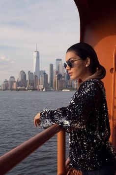 a woman standing on the side of a boat looking out at the water with a city in the background