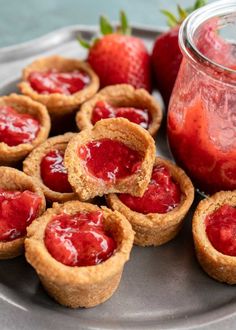 strawberry pies are arranged on a plate next to a jar of jam