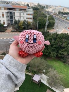 a person holding up a pink origami bird in front of a cityscape