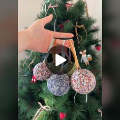 a hand is holding an ornament in front of a christmas tree with ornaments on it