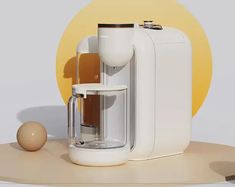 a white coffee maker sitting on top of a wooden table next to an egg shell