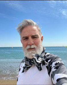 an older man with grey hair and beard standing on the beach