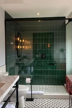 a bathroom with black and white tile on the floor, green tiled shower stall and toilet