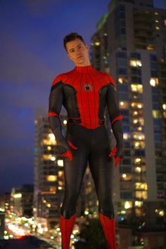 a man in a spider - man suit standing on top of a building at night