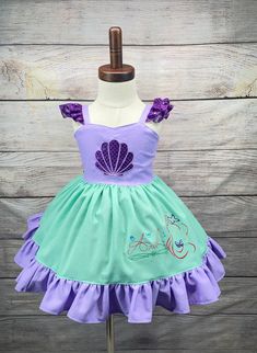 Haz realidad los sueños de tu pequeña con este encantador vestido inspirado en sirenas, inspirado en Ariel de "La Sirenita". Este vestido es la opción perfecta para cumpleaños y hará que tu niña se sienta como una verdadera princesa en su día especial. Con delicados volantes en los hombros y en el bajo de la falda, este vestido derrocha elegancia y encanto. Los detalles con volantes añaden un toque de fantasía, realzando el atractivo mágico del vestido. Tenga en cuenta que el tutú que se muestra en la foto no está incluido con el vestido. Se ha añadido debajo para una mejor presentación. Estamos orgullosos de la artesanía de nuestras prendas, y cada vestido está hecho con amor y atención al detalle. Debido a esta dedicación, el tiempo de producción de este vestido es de 3 a 5 días. Sin emb Princess Style Fitted Twirl Dress For Dress-up, Green Mermaid Hem Dress, Purple Mermaid Hem Summer Dress, Green Fitted Mermaid Dress, Fitted Fairy Dress With Ruffles For Pageant, Fitted Ruffles Fairy Dress For Pageant, Purple Mermaid Hem Dress With Ruffles, Purple Ruffle Mermaid Hem Dress, Fitted Purple Mermaid Dress With Ruffles