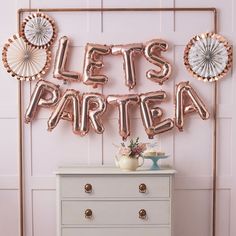 a room with balloons that say let's party on the wall and a chest of drawers