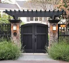 an entrance to a home with stone pillars and black gates, surrounded by greenery