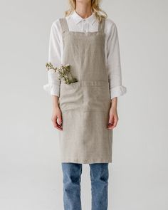 a woman wearing an apron and jeans standing in front of a white wall