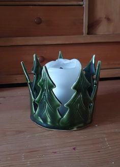 a green candle holder with trees on the sides and a white candle in the middle