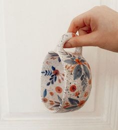 a hand holding a white and orange flowered vase with floral designs on it's side