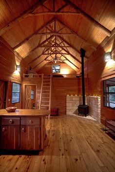 the inside of a log cabin with wood floors and exposed ceilings, an open fire place in the center