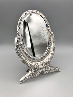 an ornately designed silver mirror on a stand with its reflection in it's center