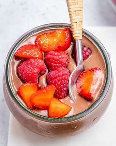 a bowl filled with chocolate pudding topped with strawberries and raspberries next to a spoon