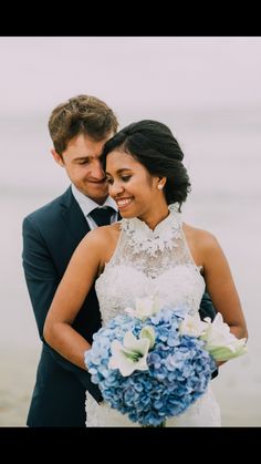 a bride and groom standing next to each other on the beach with water in the background