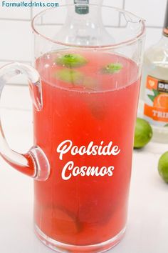 a pitcher filled with liquid sitting on top of a counter next to limes and bottles