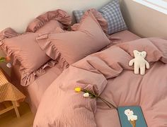 a bed with pink sheets, pillows and a teddy bear on it next to a book